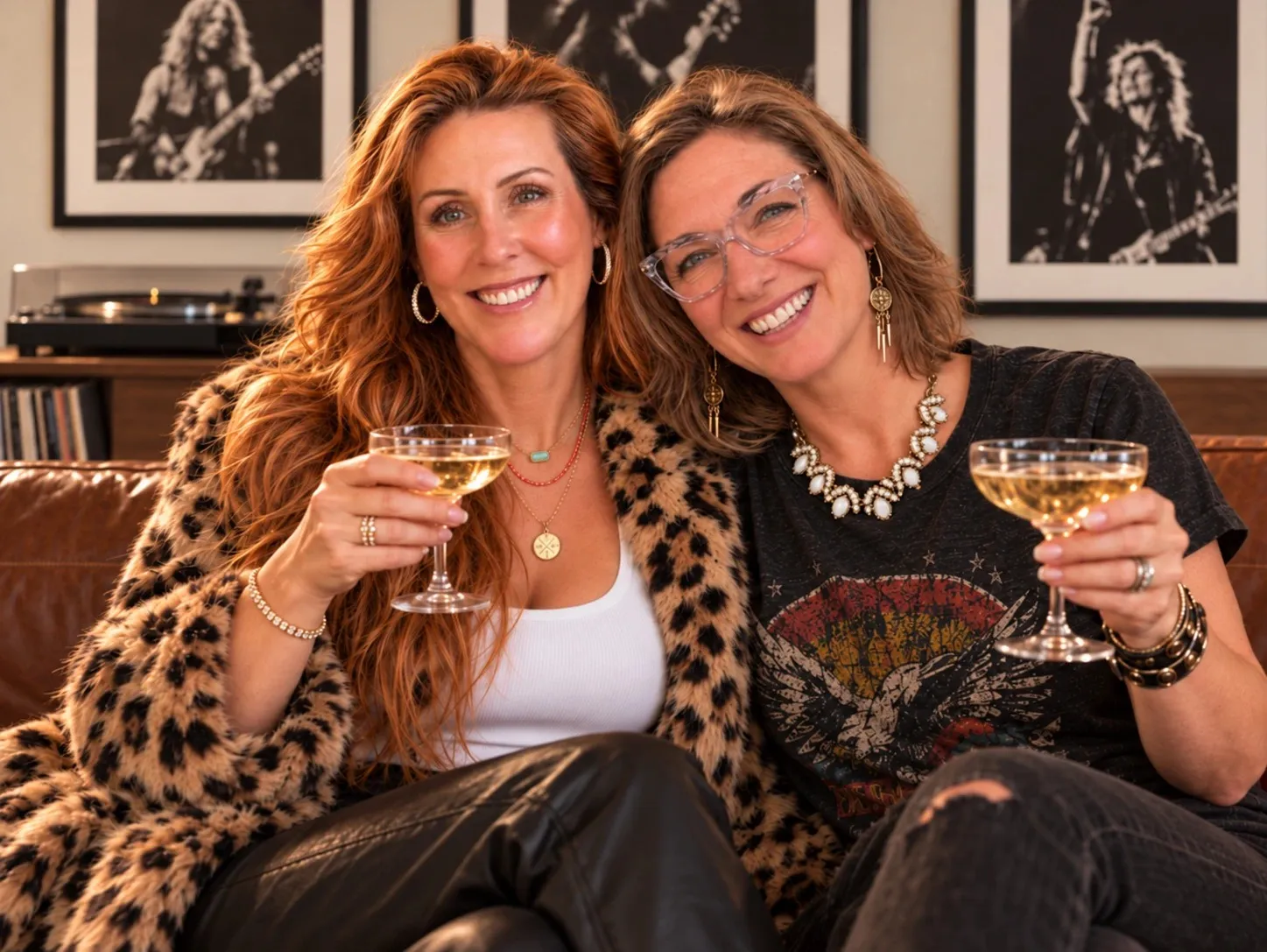 Kenda and Georgia on a leather couch, raising glasses of champagne, rock posters and a record player behind them