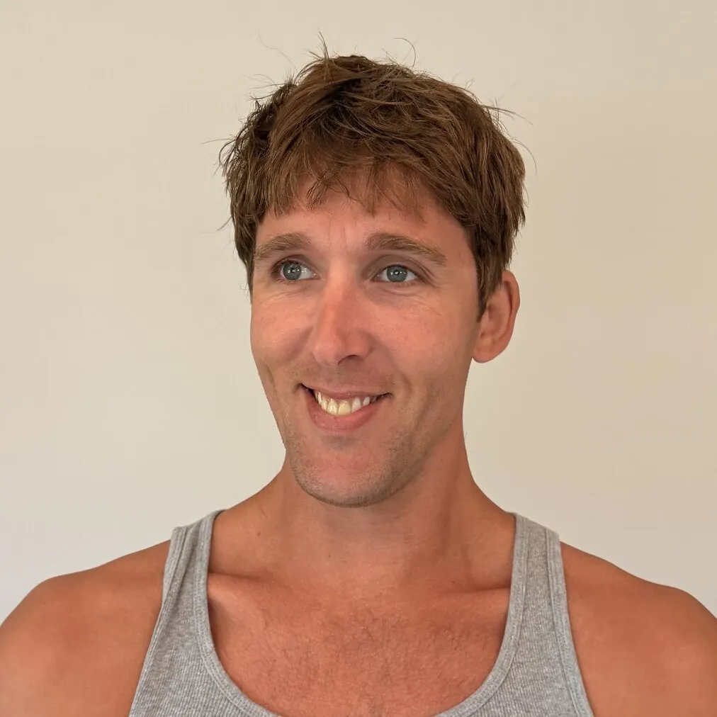 Kylen in a gray tank top against a plain wall, grinning