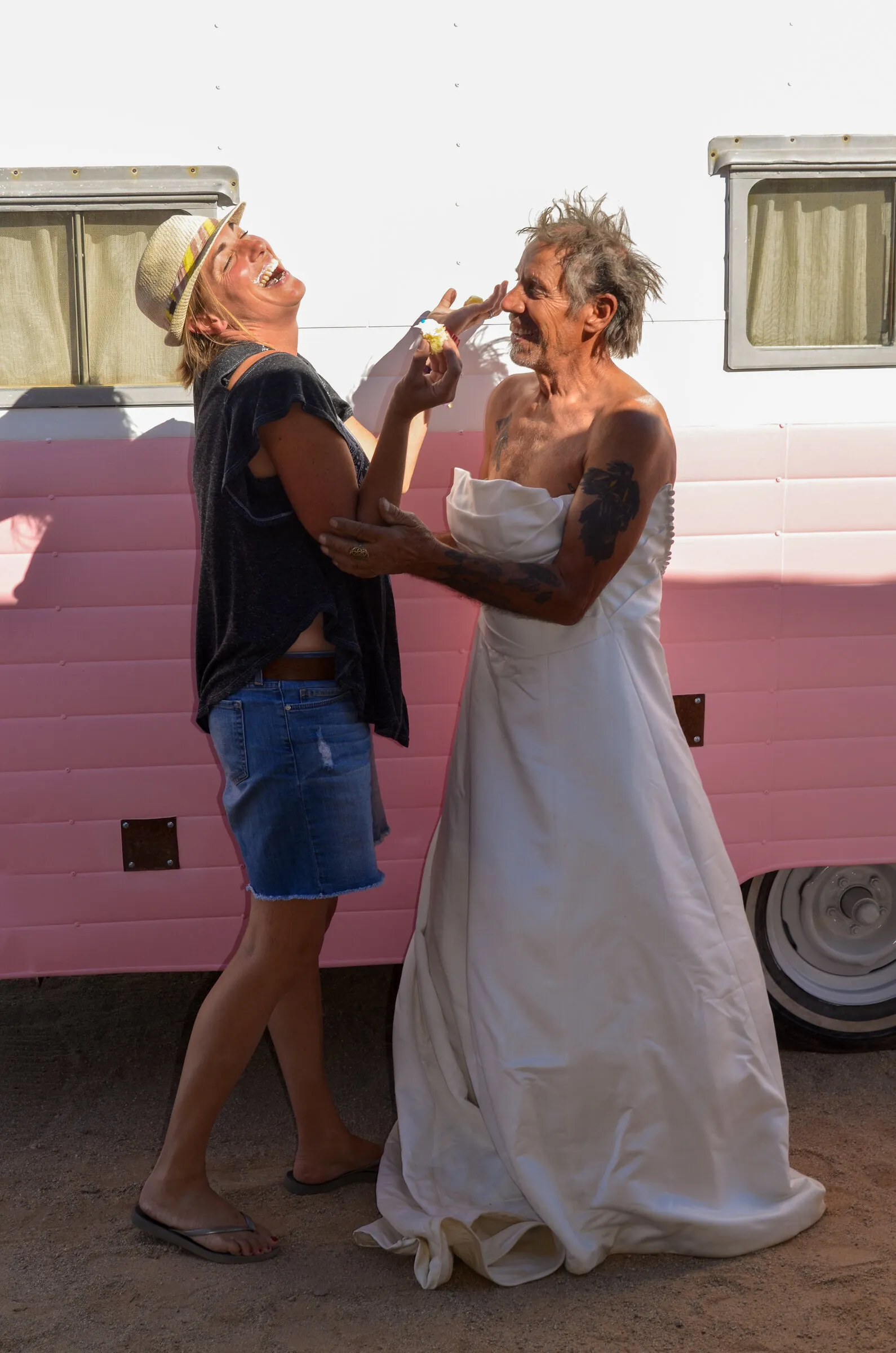 Georgia in a hat laughing with a man wearing The Divorce Dress in front of a pink trailer