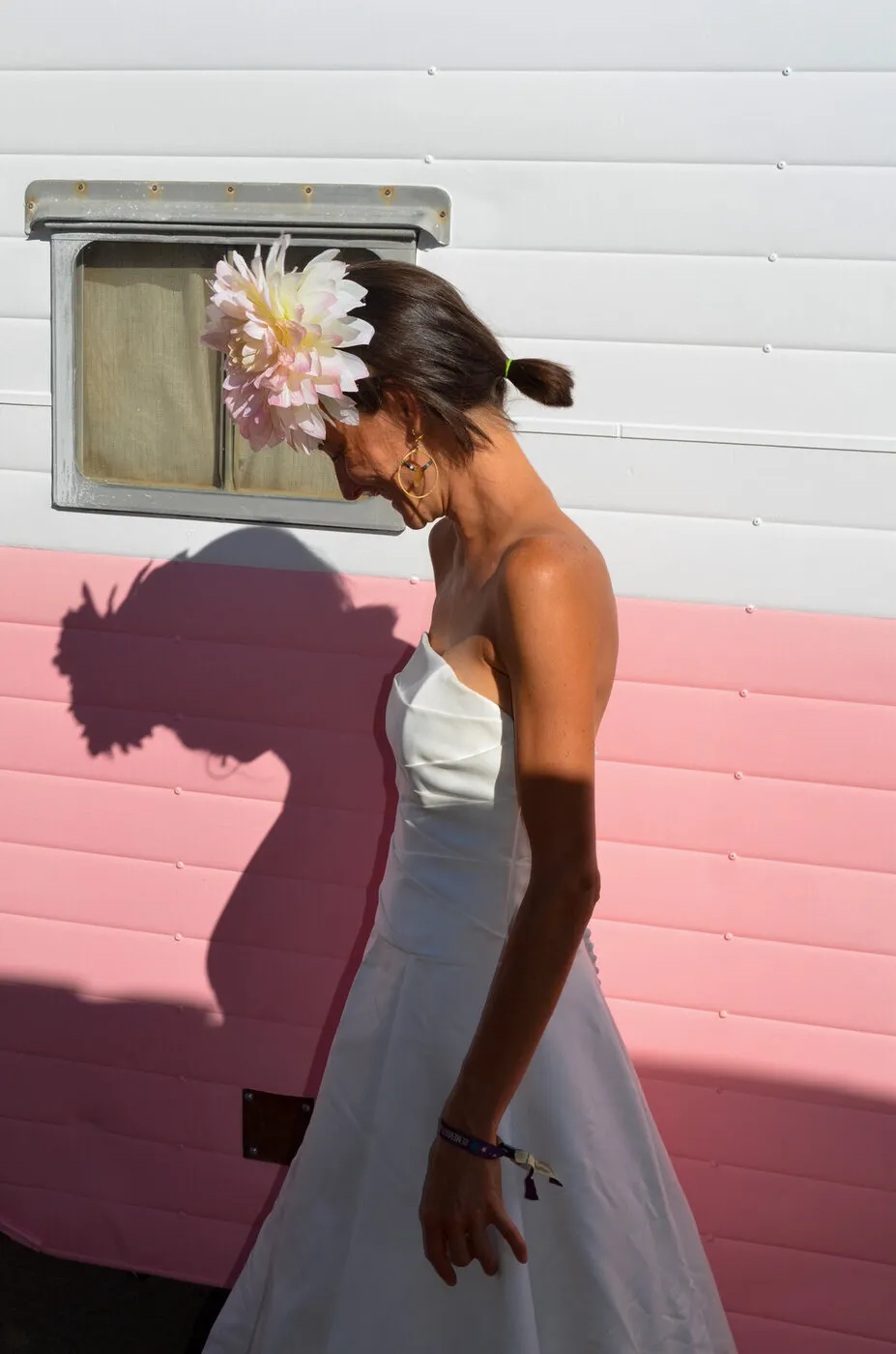 A woman in The Divorce Dress with a flower in her hair, in profile against a pink and white trailer