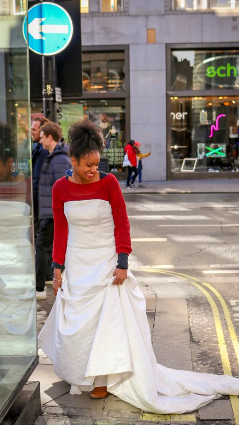 A woman in a red sweater wearing The Divorce Dress on a London street