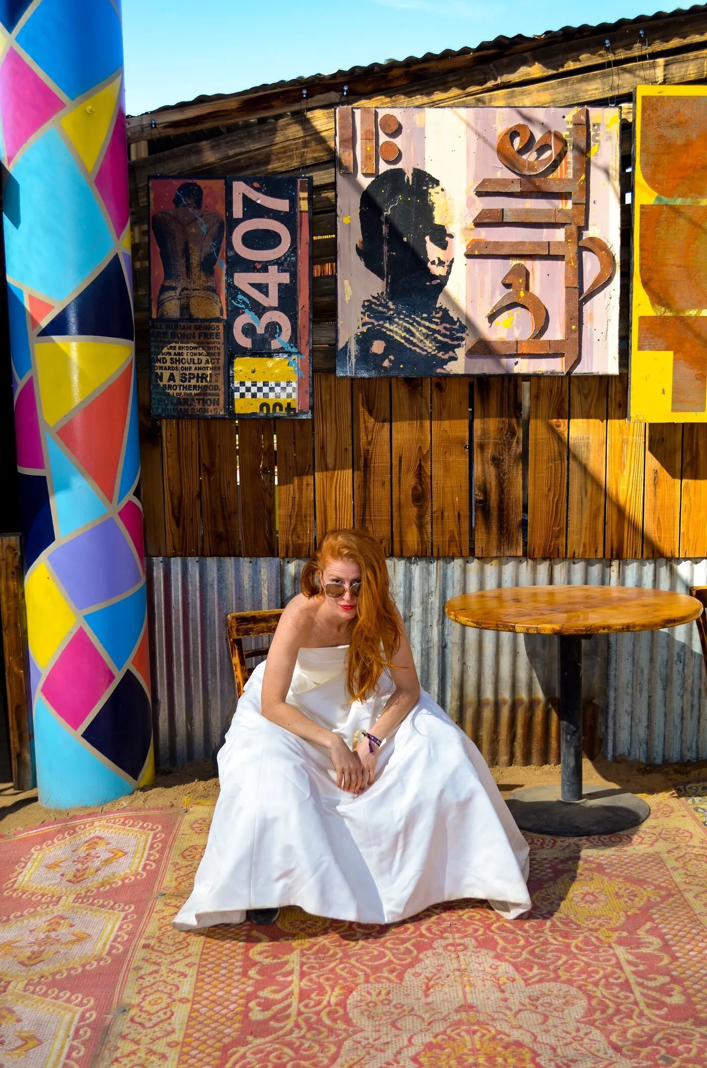 Sofia of the band Femina, with long red hair and sunglasses, in The Divorce Dress on a patterned rug in Joshua Tree