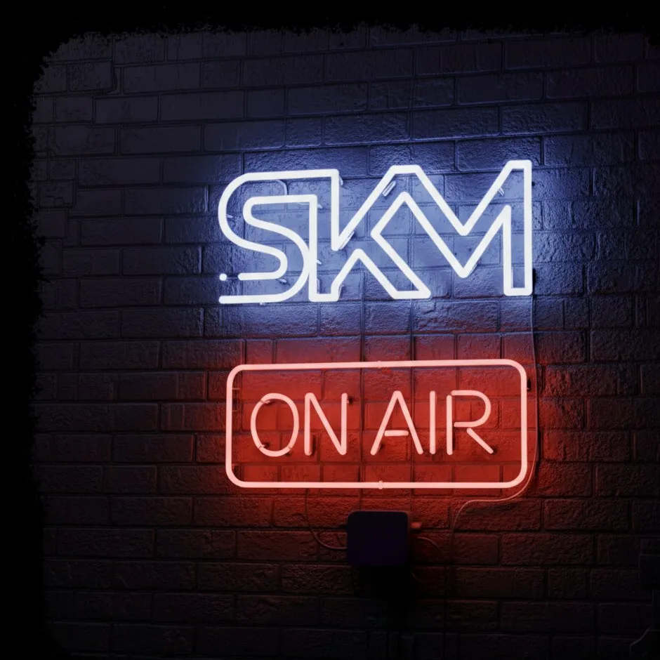 Neon SKM and ON AIR signs glowing on a dark brick wall